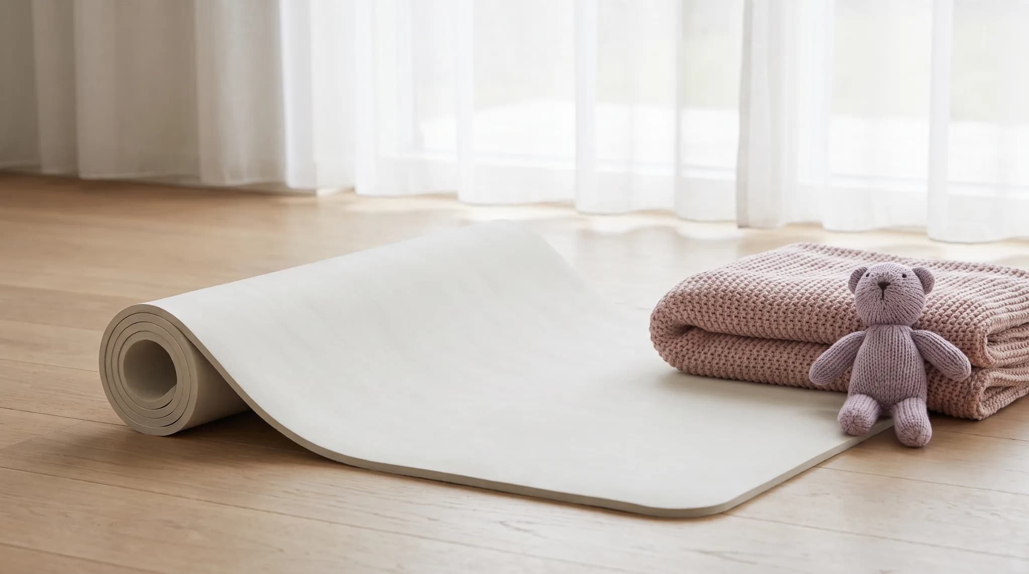 Halb ausgerollte helle Gymnastikmatte mit einer gefalteten Babydecke und einem kleinen Strickspielzeug.