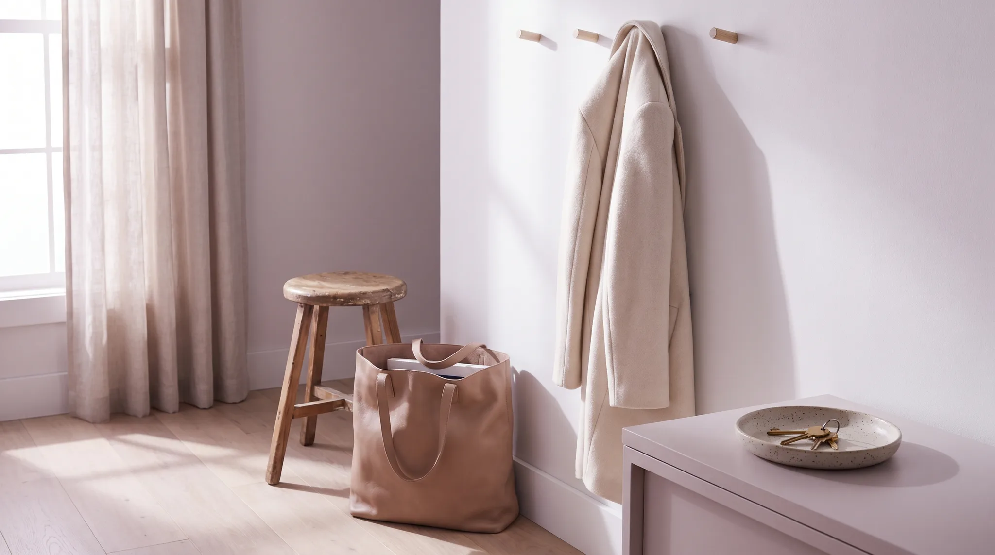 Gepackte Tasche an einer hellen Wohnungstuer, daneben ein Mantel am Haken und ein kleiner Hocker.